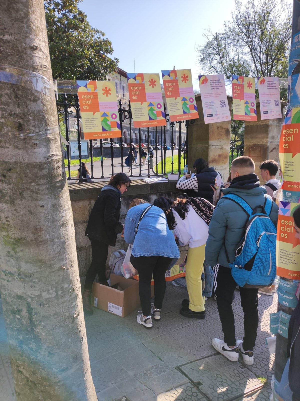Estudiantes firmando la ILP en un punto de recogida instalado en Deusto, Bilbao, rodeado de carteles de la campaña